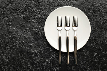 Stylish forks and plate on dark background