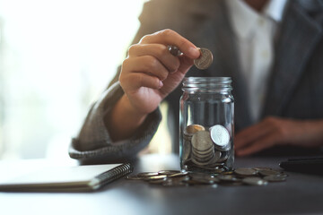 Fototapeta na wymiar Closeup image of a businesswoman collecting and putting coins in a glass jar for saving money concept