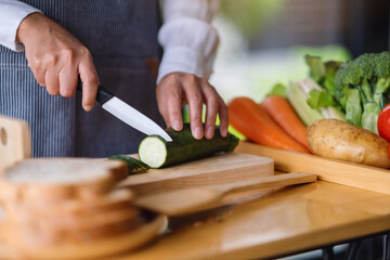 Closeup image of a female chef cutting and chopping vegetables by knife on wooden board in kitchen