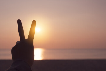 Peace out or fighting metaphor two fingers hand sign in front of a sunset.