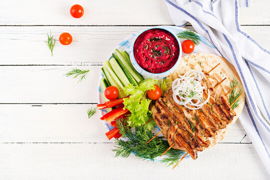 Grilled Chicken Kebab With Beet Hummus And Pita, Fresh Vegetables On A White Table.  Grilled Meat Skewers, Shish Kebab On White Background. Top View, Above, Flat Lay