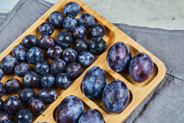 Garden plums on wooden platter with gray tablecloth