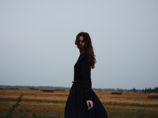 A woman in a black dress walks in the field on nature in the evening model