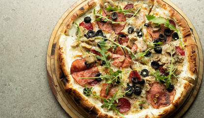 Ready Italian pizza with cheese, salami and olives on a round wooden board on the table.