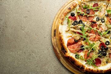 Ready hot pizza with cheese, salami and olives with fresh herbs on a round wooden board on a gray...