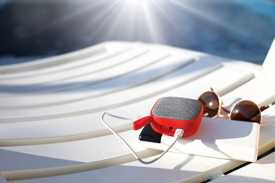 Red Music Portable Speaker Is Charged From The Power Bank Via Usb On A Deck Chair Near The Pool. Concept Is Always In Touch, Travel Gadgets, External Battery For A Smartphone. Place For Text. Flatlay