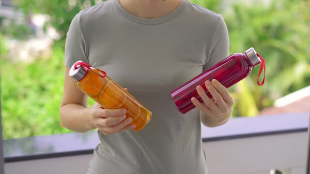 A woman holds two bottles with kombucha drink in her hands, which have different flavors - orange and dragon fruit. Healthy drinks concept