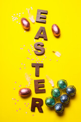 Word Easter and sweet chocolate eggs on color background