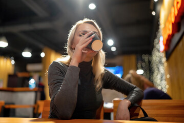 Young beautiful blonde girl drinks coffee in the evening in a cafe.
