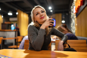 Young beautiful blonde girl drinks coffee in the evening in a cafe.