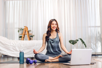 Portrait of sport asian woman in sportswear sitting relax and practicing yoga and do fitness exercise with laptop computer in bedroom at home.Diet concept.Fitness and healthy lifestyle