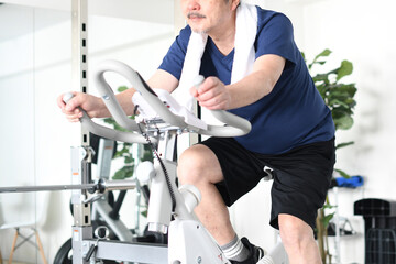 ジムでエアロバイクを漕ぐ白髪で笑顔のシニア男性
