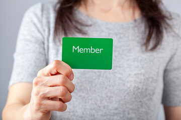 A young caucasian woman is holding a green card that says member on it. A customizable image which has space for text to be inserted. Being a member, membership dues, subscription, group concepts.