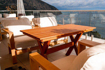 Restaurant with sea view. You can see rocks in the sea. Wooden tables and chairs with white cushions. Overcast, cloudy weather.