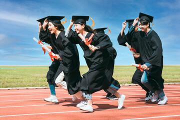 happy graduation students  holding diploma and running on the stadium at school