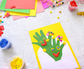 Child made  greeting card from envelope, paper own palms and decoration clay, plasticine as gift for Mothers day, Birthday or Valentines day . Arts  crafts concept.
