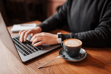 Handsome man working on laptop in the workplace. Businessman prints information at desk with coffee