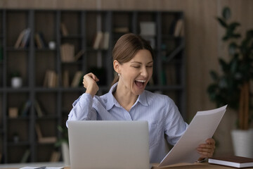 Overjoyed young Caucasian woman work on computer at home office triumph read good news in postal...