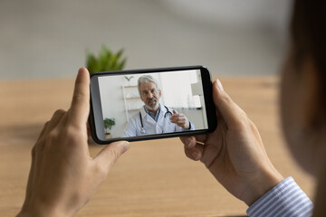 Back view close up of woman look at cellphone screen have online consultation with make mature doctor. Female speak talk on video call on smartphone with elderly GP, consult about health problem.