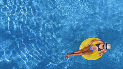 Beautiful woman in hat in swimming pool aerial view from above, young girl relaxes and has fun on inflatable ring in water on vacation
