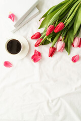 Pink tulips, coffee cup and books view on white bed
