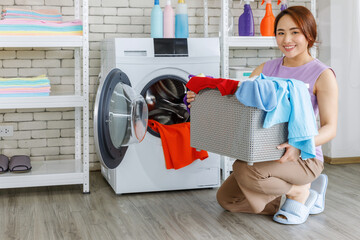 Happy Asia woman holding laundry basket in the utility room near washing machine at home.