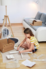 Fototapeta na wymiar Little girl assembling furniture in a new home - moving into a new home concept.