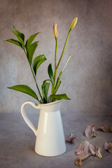 Dry wilted tulip flowers and green plants on a white vase and leaves on a grey vintage background.