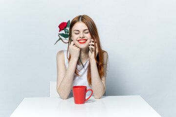 woman sitting at the table drinking from a red mug and talking on the phone