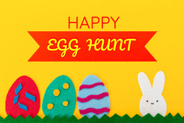 Easter. Cut out of felt applications of eggs and a rabbit on the grass. Yellow background. Flat lay