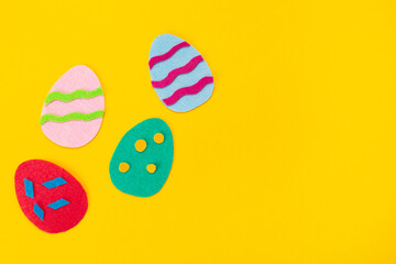 Easter decorations. Cut out of felt applications of colourful eggs on yellow background. Flat lay. Copy space