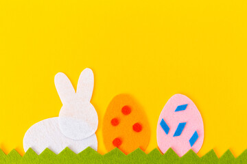Cut out of felt applications of two colourful eggs and silhouette white rabbit on the grass. Yellow background. Flat lay. Easter holiday. Copy space