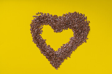 Flax seeds in the shape of a heart on a yellow background