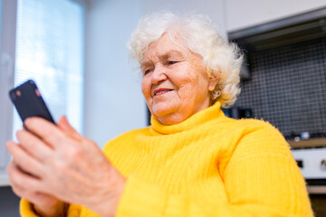 Portrait of old smiling lady looking at screen of mobile phone
