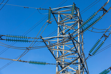 New large mast of an air power line close up, high voltage electricity pylon with thick wires and insulators, blue sky on background. Traditional energy. Electric power concept.