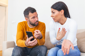 Boyfriend asking for an explanation to his cheater sad girlfriend sitting on a couch in the living...