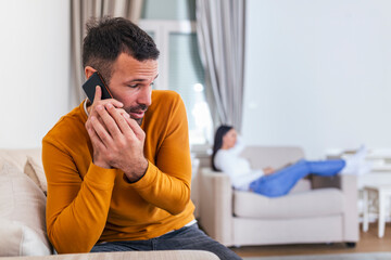Handsome young man cheating on girlfriend talking with lover while she is watching tv in the...