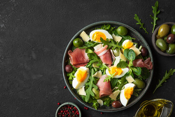Salad with prosciutto, parmesan, olives, eggs and arugula in a plate on a dark background. Italian food. top view