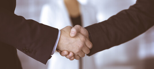 Obraz premium Unknown businesspeople are shaking their hands after signing a contract, while standing together in a modern office, close-up. Business communication, handshake, and marketing concept