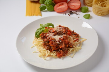 Traditional Italian spaghetti Bolognese  served on a white plate with tomatoes and basil