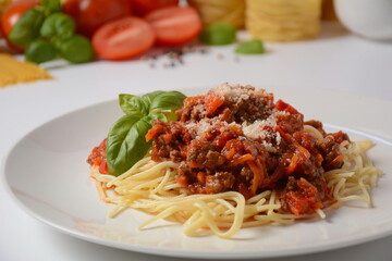 Traditional Italian spaghetti Bolognese  served on a white plate with tomatoes and basil