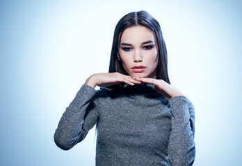 An elegant lady in a gray sweater gestures with her hands with makeup and eyeshadows