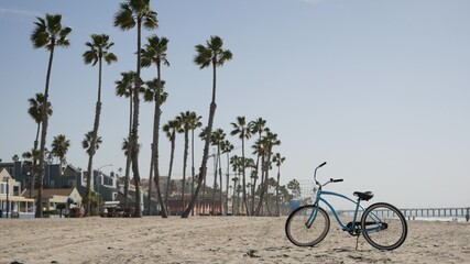 Fototapeta premium Blue bicycle, cruiser bike by sandy ocean beach, pacific coast near Oceanside pier, California USA. Summertime vacations, sea shore. Vintage cycle, tropical palm trees, lifeguard tower watchtower hut