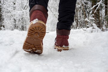 A man in boots is walking through the winter forest. Bottom view of shoes, selective focus. Concept of hikes walks and winter holidays
