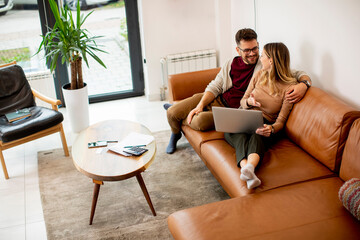 Obraz premium Young couple using laptop together while sitting on sofa at home