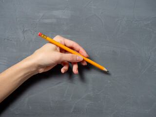 A woman holds a pencil in her left hand on a gray textured background. The concept of the artist, left-handed