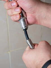 Broken chrome shower hose in men's hands. Rift, rubber, selective focus, shower equipment, vertical photo
