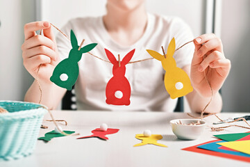 DIY Easter home decor. Happy boy make garland of colored paper, twine and pom-poms. Selective focus