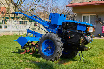 Obraz premium blue two wheeled tractor,new tractor with a spring cultivator stands in the yard