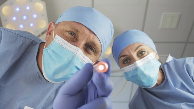 Surgery, at hospital. Patient wakes up after a coma. Doctor with assistant checks reaction of the pupils of the eyes with flashlight. First-person view